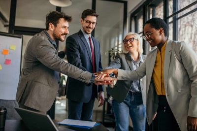 Group of diverse businesspeople holding hands together, united in new projects and ideas while standing in the bright office.